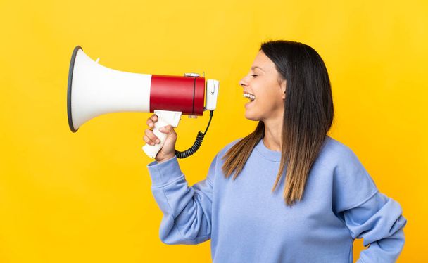 Caucasian girl isolated on yellow background shouting through a megaphone to announce something in lateral position - Photo, image