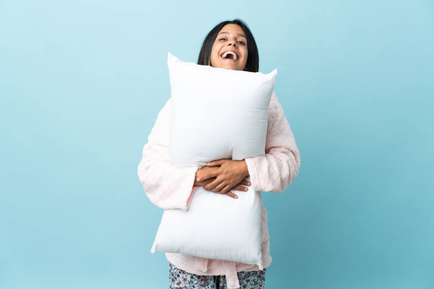 Junge Frau im Schlafanzug über isoliertem Hintergrund im Schlafanzug und mit einem Kissen mit glücklichem Gesichtsausdruck - Foto, Bild