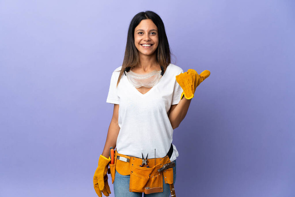 Young electrician woman isolated on purple background pointing to the side to present a product - Photo, image
