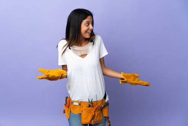 Young electrician woman isolated on purple background with surprise expression while looking side - 写真・画像