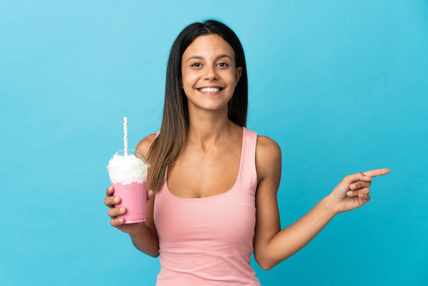 Young woman with strawberry milkshake pointing finger to the side - Foto, Imagem