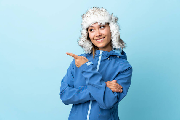 Молода уругвайська дівчина з зимовим капелюхом на синьому фоні вказує пальцем на бік. - Фото, зображення