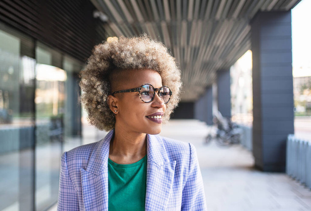 Νεαρή εμπνευσμένη Αφρο-Αμερικανίδα επιχειρηματίας κοιτάζει στο πλάι. Χαρούμενη επιτυχημένη μαύρη επαγγελματίας. - Φωτογραφία, εικόνα