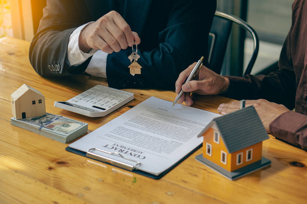 Ingatlanügynökök, értékesítési menedzserek kulcsokat osztanak ki az ügyfeleknek, miután bérleti szerződést vagy lakásvásárlási megállapodást írtak alá egy lakáshitel- és lakásbiztosítással az asztalnál.. - Fotó, kép