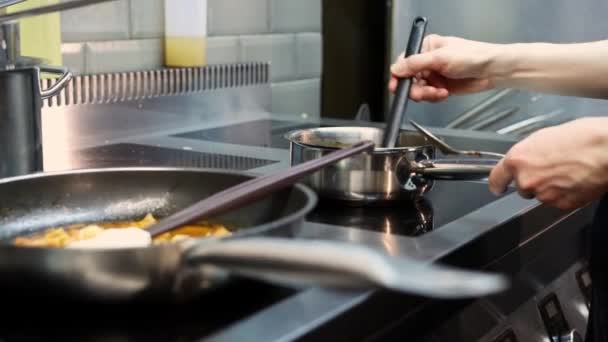 Chef sacude una cacerola en una estufa eléctrica y mezcla el contenido - Imágenes, Vídeo