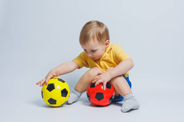 Kibic trzymający piłkę w rękach, odizolowany na białym tle. Nowe dziecko w futbolu, sport dla dzieci. Mały sportowiec. Żółty i niebieski zestaw do piłki nożnej dla dzieci - Zdjęcie, obraz