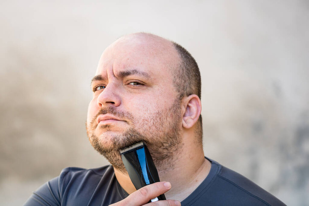 Mężczyzna golący lub przycinający brodę za pomocą maszynki do strzyżenia włosów lub maszynki do golenia elektrycznego - Zdjęcie, obraz