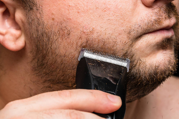 Mann rasiert oder schneidet sich den Bart mit Haarschneidemaschine - Foto, Bild