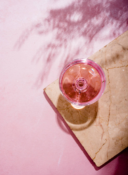 Pink champagne in glass on luxury marble table with palm shadow. Summer beach cocktail party with  rose wine alcohol beverage on textured background with tropical plant shade. Top view. - Fotoğraf, Görsel
