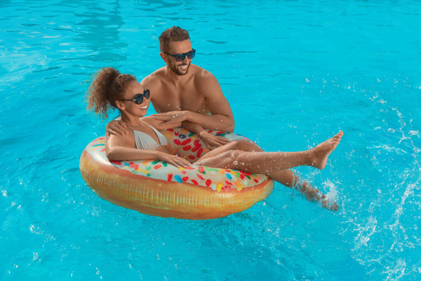 Happy couple with inflatable ring in outdoor swimming pool on sunny summer day - Фото, зображення