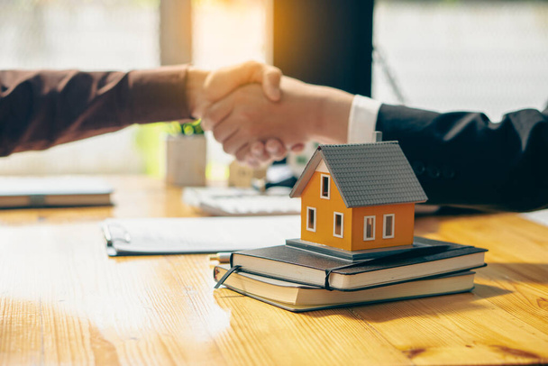 The orange house on tigerskin and the sales representative and the new homeowner join hands to sign a contract to buy the house or rent on the workspace table. moving concept - Photo, Image