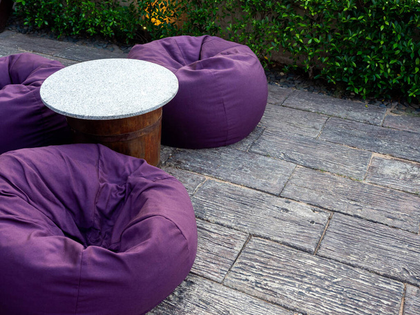 Tyhjä pyöreä marmori alkuun pöytä kolme violetti papu pussit kopio tilaa maassa lähellä vihreä pensas, ulkona puutarha koristelu. - Valokuva, kuva