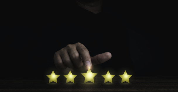Gold five stars point, best excellent rating satisfaction pointing by the finger of man in black on dark background. Banner for customer service evaluation, client experience survey concept. - Photo, Image