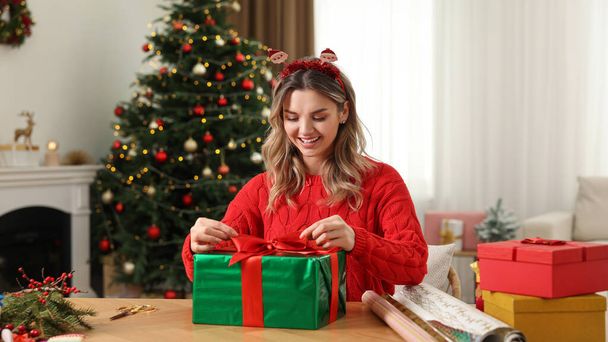 Beautiful young woman wrapping Christmas gift at home - Фото, зображення