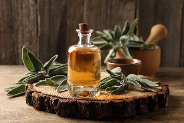 Bottle of essential sage oil and twigs on wooden table - Fotografie, Obrázek