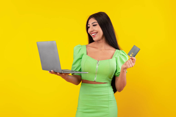 Mujer joven emocionada sosteniendo tarjeta de crédito y portátil - Foto, Imagen