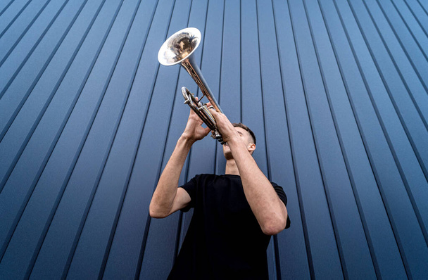 Young street musician playing the trumpet near the big blue wall - Foto, afbeelding