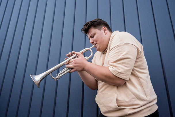 Young street musician playing the trumpet near the big blue wall - Fotó, kép