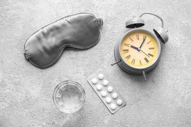 Маска для сну, будильник, склянка води і таблетки на сірому фоні
 - Фото, зображення