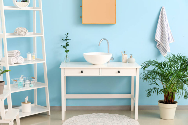 Interior of stylish bathroom with sink, shelving unit and blue wall - Foto, Bild