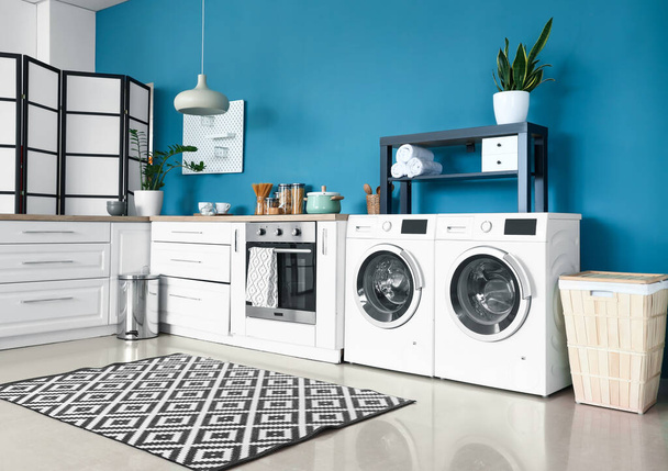 Интерьер стильной кухни с современными стиральными машинами, духовкой и белыми прилавками - Фото, изображение