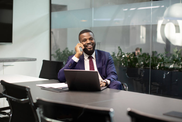 Positive black manager working on computer, having phone conversation - Foto, imagen
