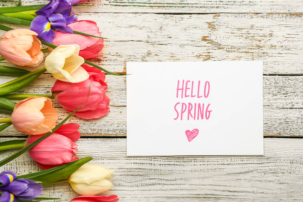Card with text HELLO SPRING and beautiful flowers on light wooden background - Fotó, kép
