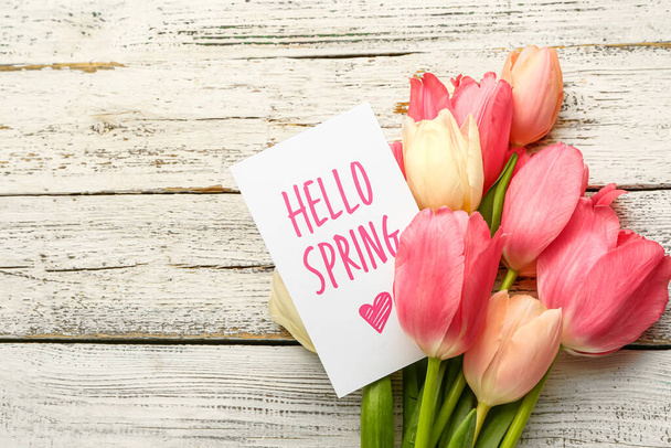 Card with text HELLO SPRING and bouquet of tulip flowers on light wooden background, closeup - Fotoğraf, Görsel
