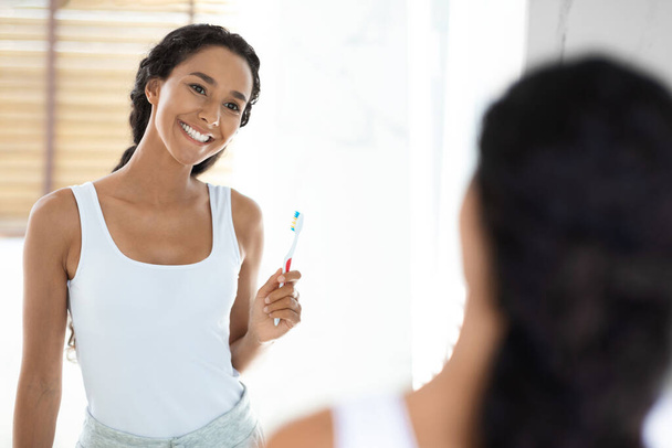 幸せな若い女性は歯ブラシを保持し、バスルームでミラーを見て - 写真・画像