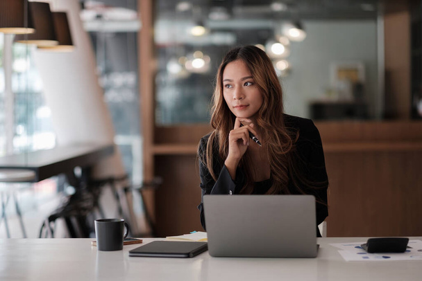 Азійська красива жінка, яка думає і працює з ноутбуком для фінансового забезпечення в сучасному офісі - Фото, зображення