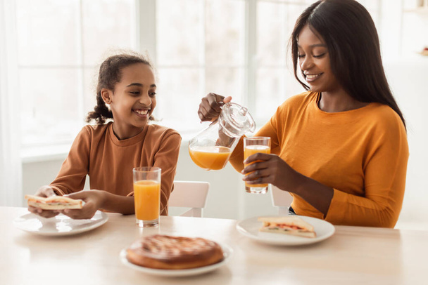 Allegro nero madre e figlia bere arancia succo in cucina - Foto, immagini