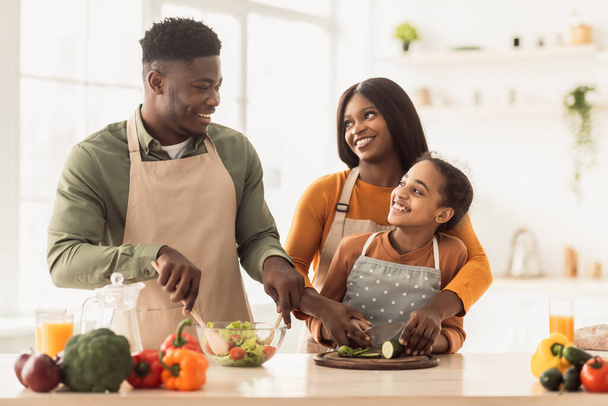 Afrikanische Eltern und Tochter kochen gemeinsam Salat in der Küche - Foto, Bild