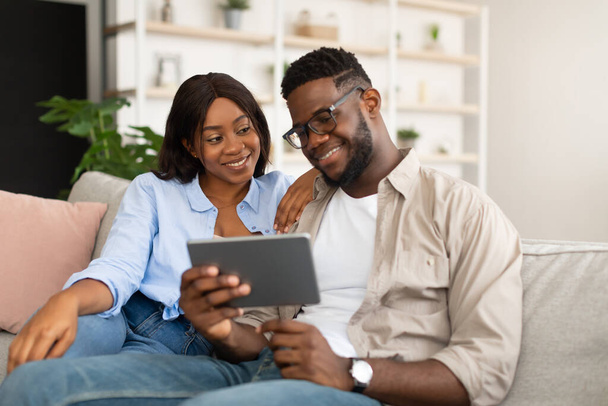 Adorável casal afro-americano sentado no sofá, usando tablet - Foto, Imagem