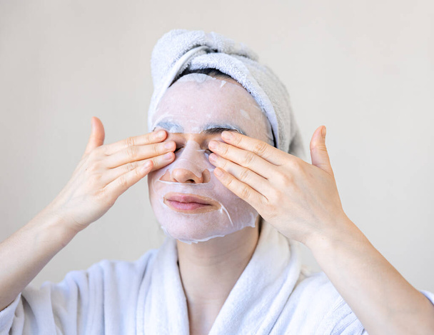 Mujer joven con máscara de sábanas en la cara, procedimiento de spa. - Foto, imagen