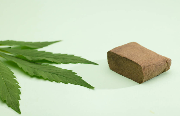 Großportion Haschisch-Tablette mit Marihuana-Blatt, grüner Hintergrund - Foto, Bild