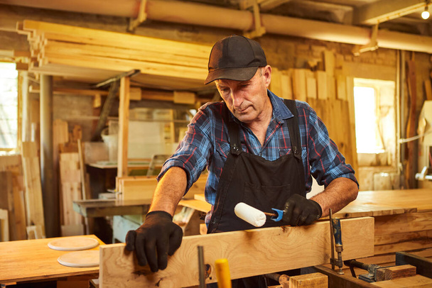 Retrato de un carpintero mayor en barras de madera de encolado uniforme con presiones de mano en la fabricación de carpintería - Foto, imagen