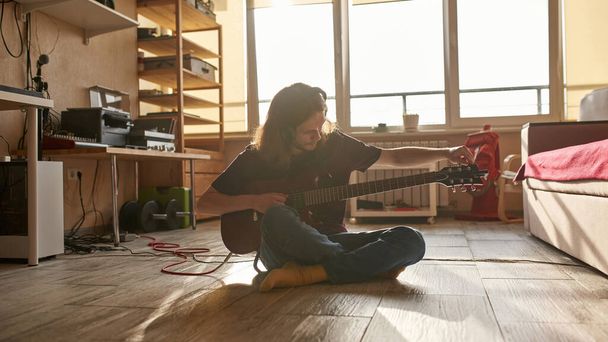 Man tuning guitar before playing on floor at home - Φωτογραφία, εικόνα