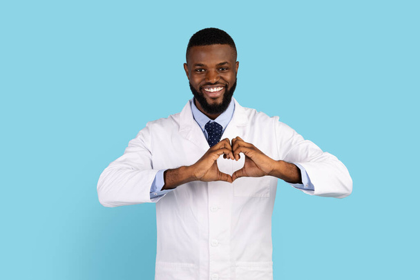 Uśmiechnięty Afroamerykanin mężczyzna lekarz w mundurze robi znak serca z rąk - Zdjęcie, obraz