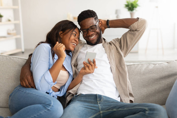 African american couple sitting on couch, using cellphone - Photo, Image