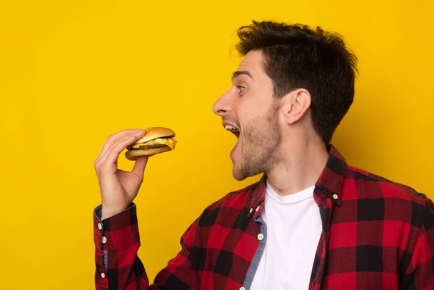 drôle affamé gars tenant burger mordant sandwich au studio - Photo, image