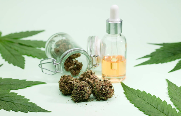 Marijuana buds, glass jars with corks and marijuana indoors, green leaves, green background. - Foto, immagini