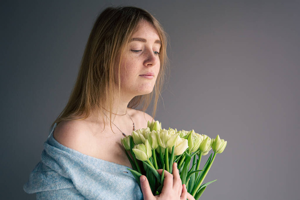 灰色の背景にチューリップの花束を持つ若い女性の肖像画. - 写真・画像