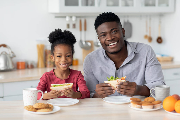Vrolijke zwarte vader en kind met snack thuis - Foto, afbeelding