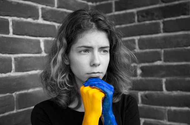 black - white portrait of a sad young woman, hands painted in colors of Ukrainian flag. Color accent on yellow and blue. Stop the war. Hope and faith. Fear and powerlessness. Stand with Ukraine - Photo, Image