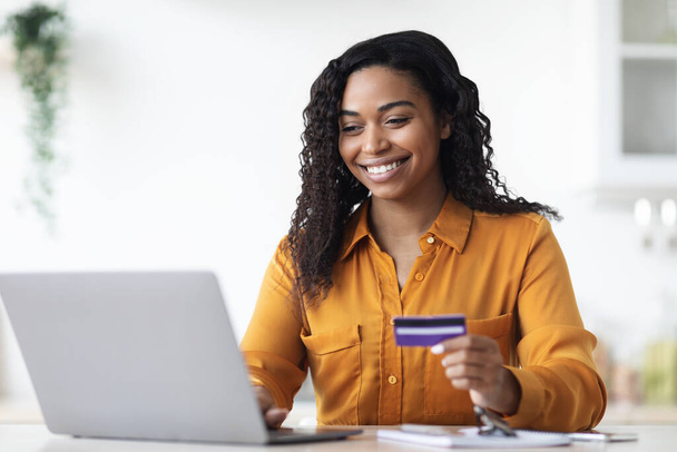 Pozytywne młoda czarna kobieta za pomocą laptopa, trzymając kartę kredytową - Zdjęcie, obraz