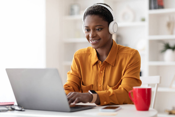 Attractive black woman attending webinar, using laptop and headset - Foto, Imagen