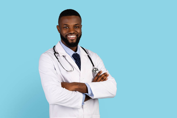Медицинские услуги. Симпатичный чёрный мужчина-доктор в униформе, позирует со сложенными руками - Фото, изображение