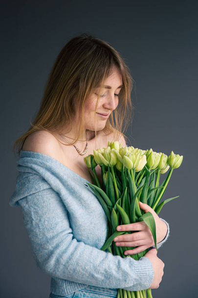 Portrait of a young woman with a bouquet of tulips on a gray background. - Фото, изображение