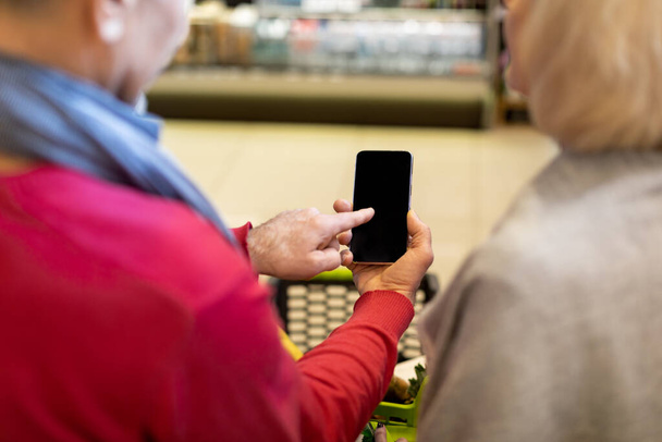 Неузнаваемая пожилая пара, использующая смартфон во время шоппинга - Фото, изображение