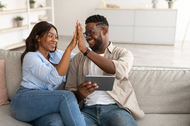Africano americano pareja usando tableta, celebrando ganar dando alta cinco - Foto, Imagen